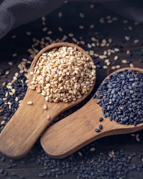 White and black sesame seeds in wooden spoons